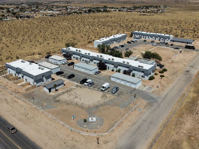 Aerial view of Apple Valley Townhomes: ten low two-story buildings with grey tile roofs, garages and playground at the front along Sioux Road, fenced backyards behind each row