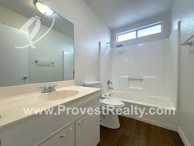 A bathroom with a tub and shower, a vanity with a wide mirror, and a window over the tub